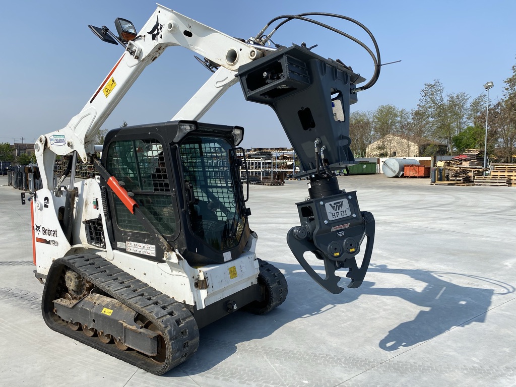 left angled view of a skid steer parked on concrete with a VTN scrap sheer attachment on the front lifted up and tilted down