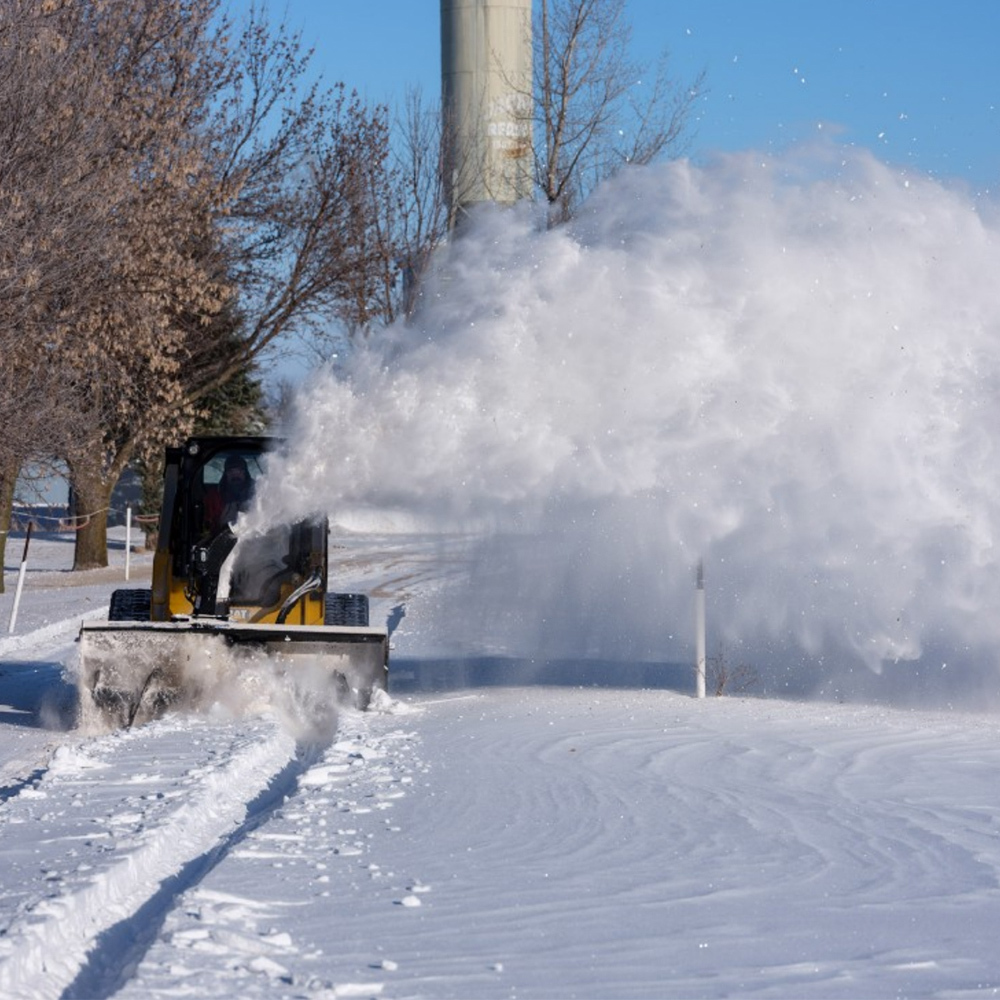 front distant view of a skid steer with a blue diamond skid steer snow blower attachment on the front blowing snow