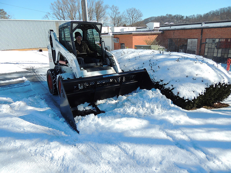 left angled view of skid steer with a blue diamond skid steer high back snow bucket attachment on the front pushing snow