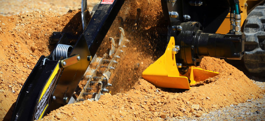 closeup view of a digga skid steer trencher attachment trenching into the dirt