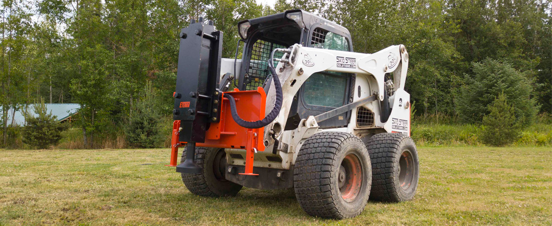 right angled view of a skid steer parked on grass with an eterra skid steer pdx post driver attachment on the front