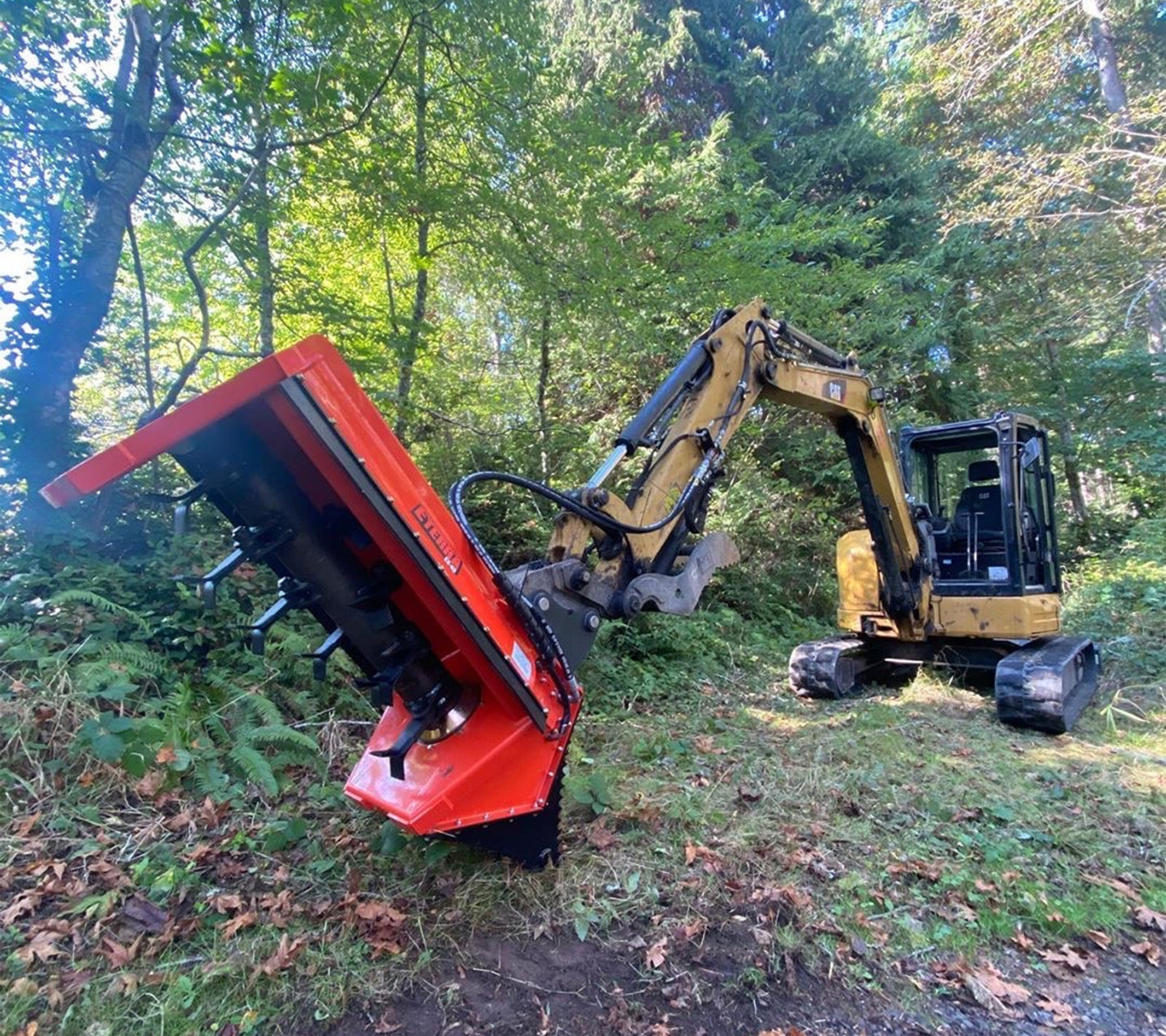 front angle view of an excavator parked in a forested area with an eterra ex-30 excavator flail mower attached to the boom