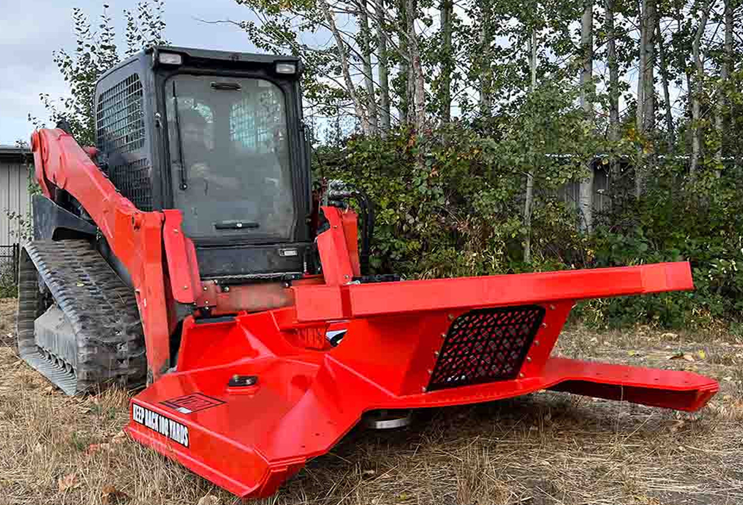 right side view of a skid steer parked in a forested area with an eterra skid steer typhoon clearing mower attachment on the front slightly raised