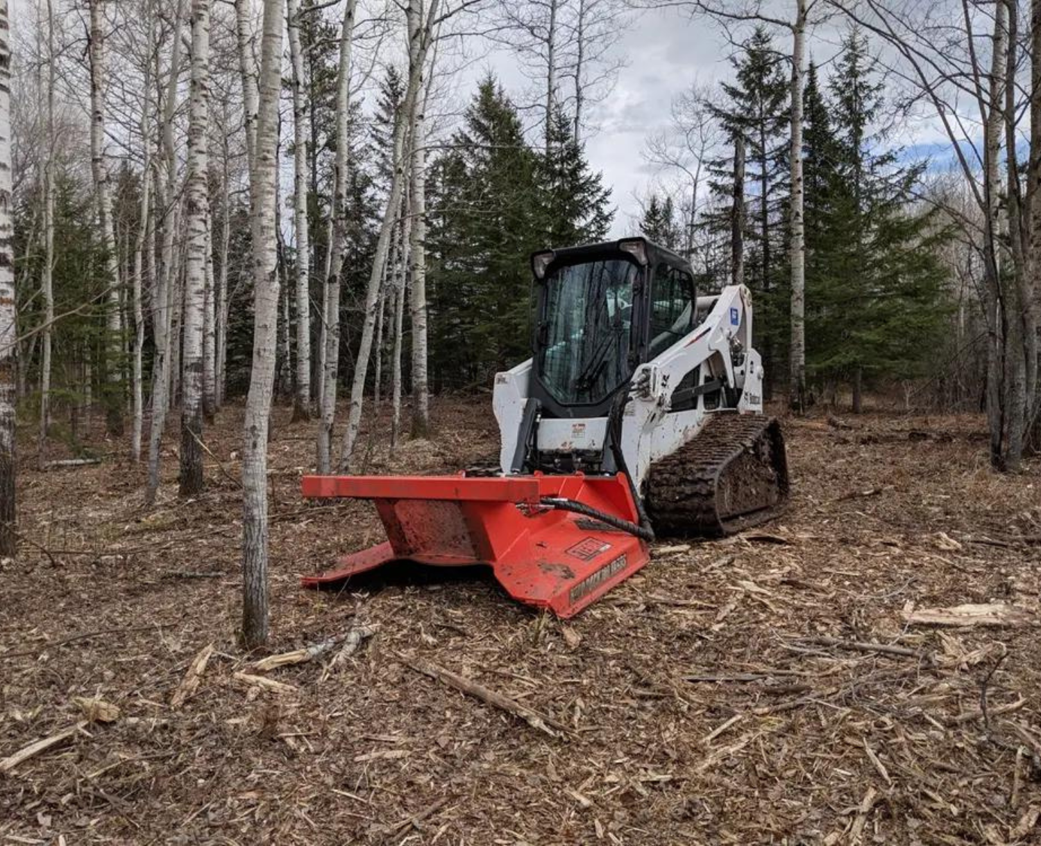 right angled view of a skid steer parked in a forested area with an eterra skid steer typhoon clearing mower attachment on the front
