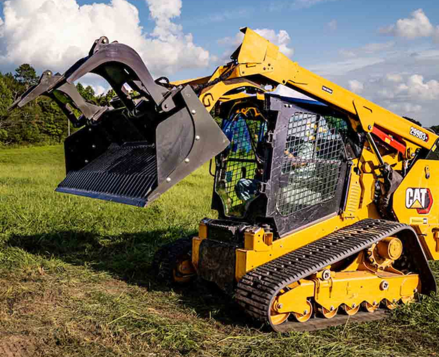 right angled view of a skid steer parked on grass with a CID skid steer rock grapple attachment on the front, lifted and open