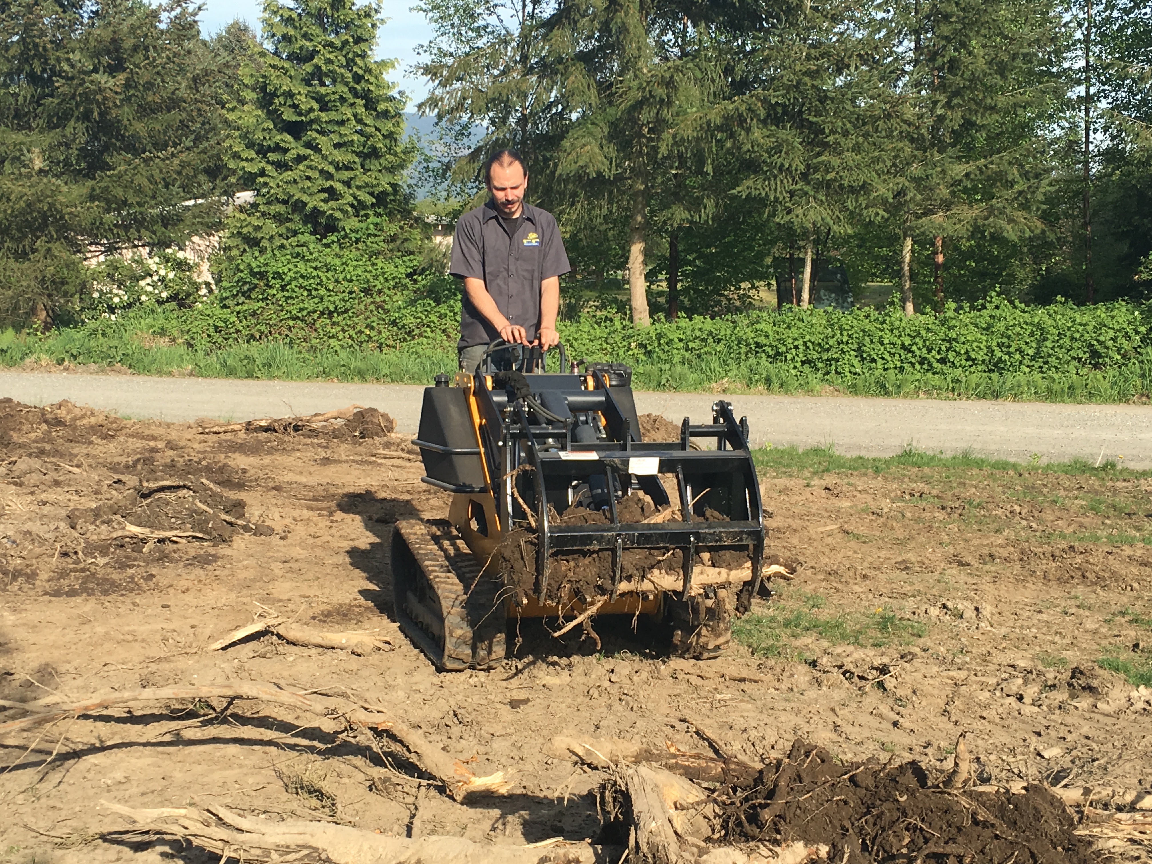 left angled view of a mini skid steer being operated by a man with a mini skid steer grapple attachment on the front