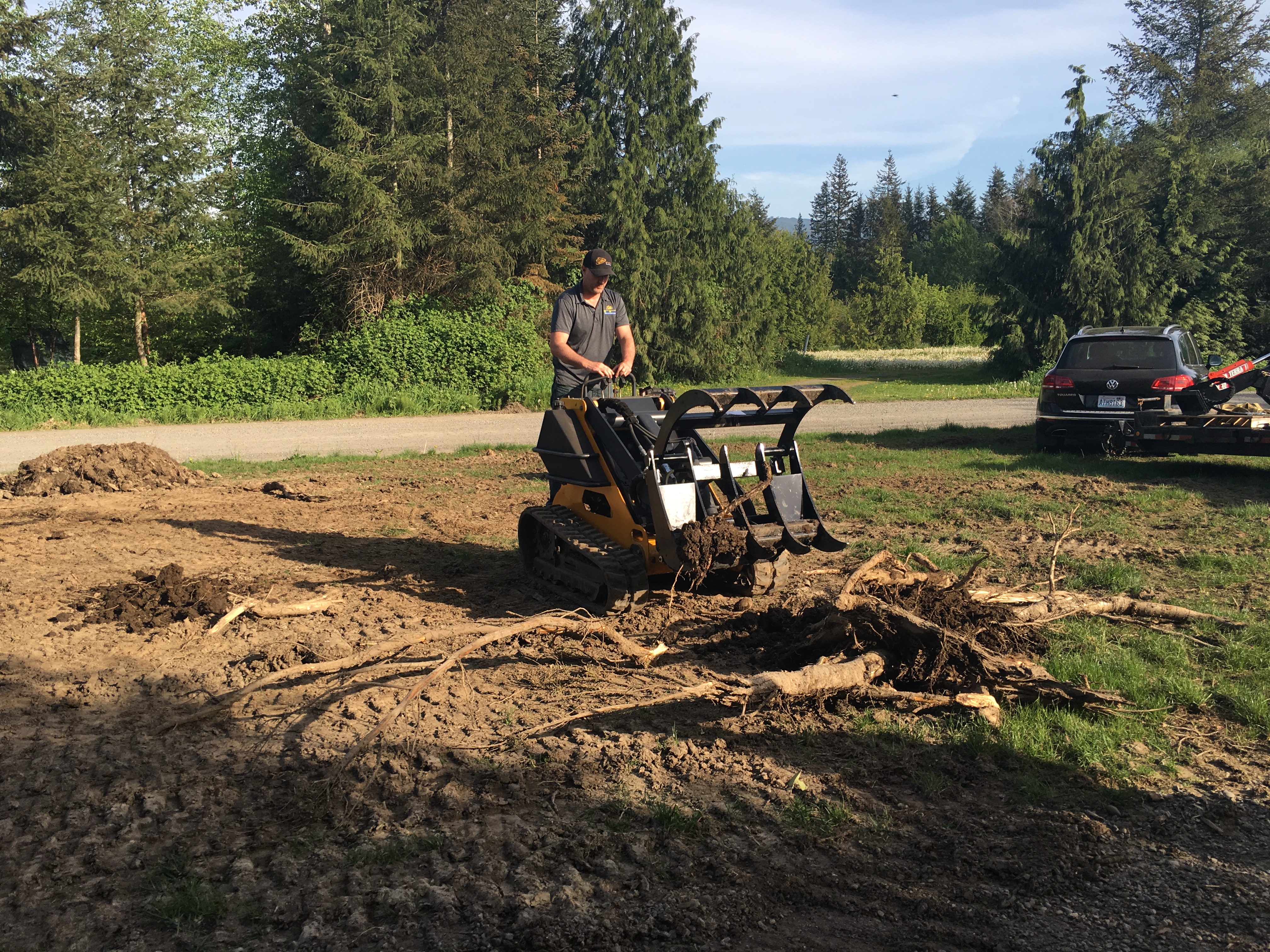 wide shot of a mini skid steer parked at a left angle with a man operating it with a mini skid steer grapple attachment on the front