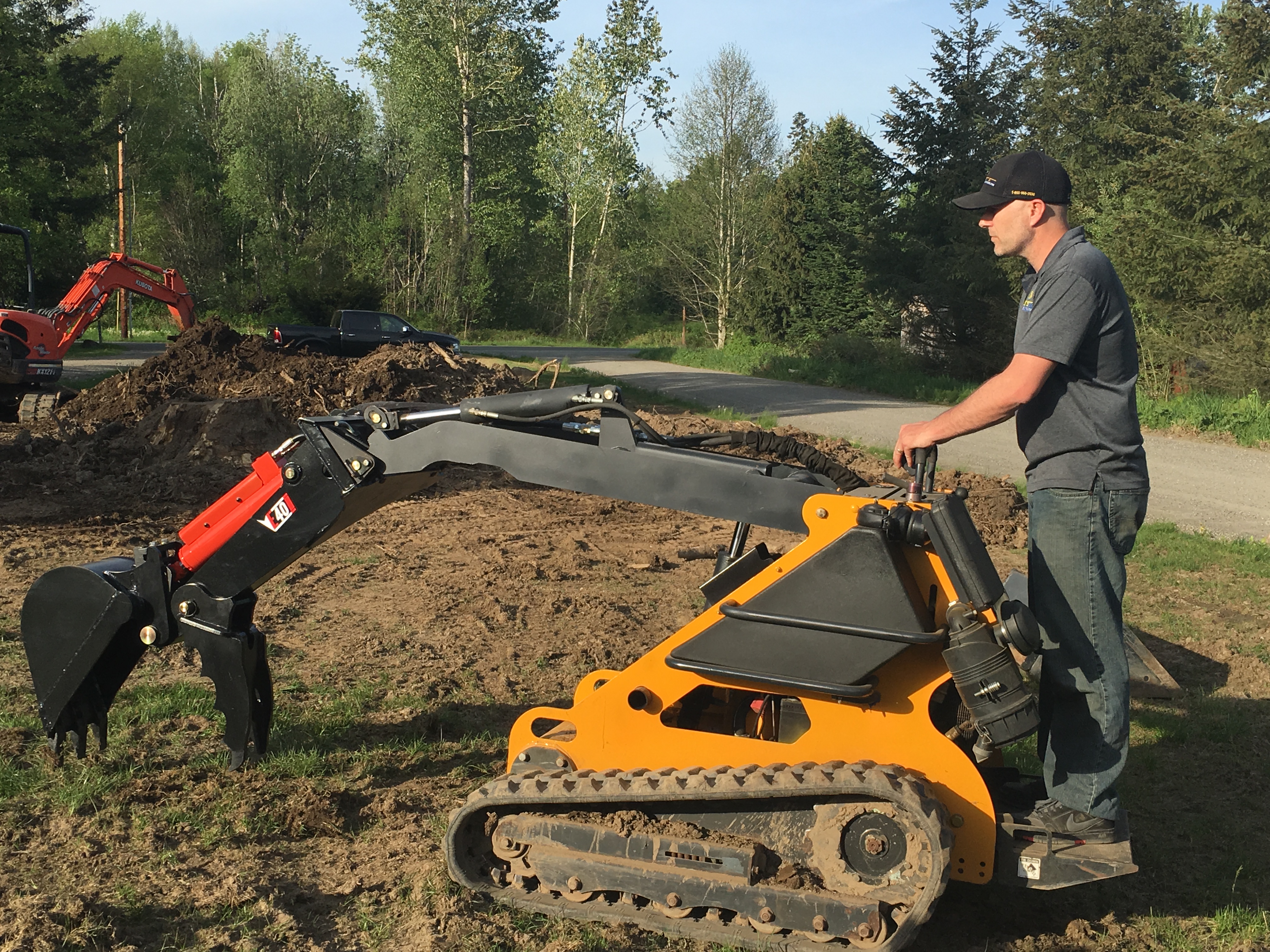 side view of a mini skid steer being operated by a man with an eterra mini skid steer backhoe attachment scooping dirt