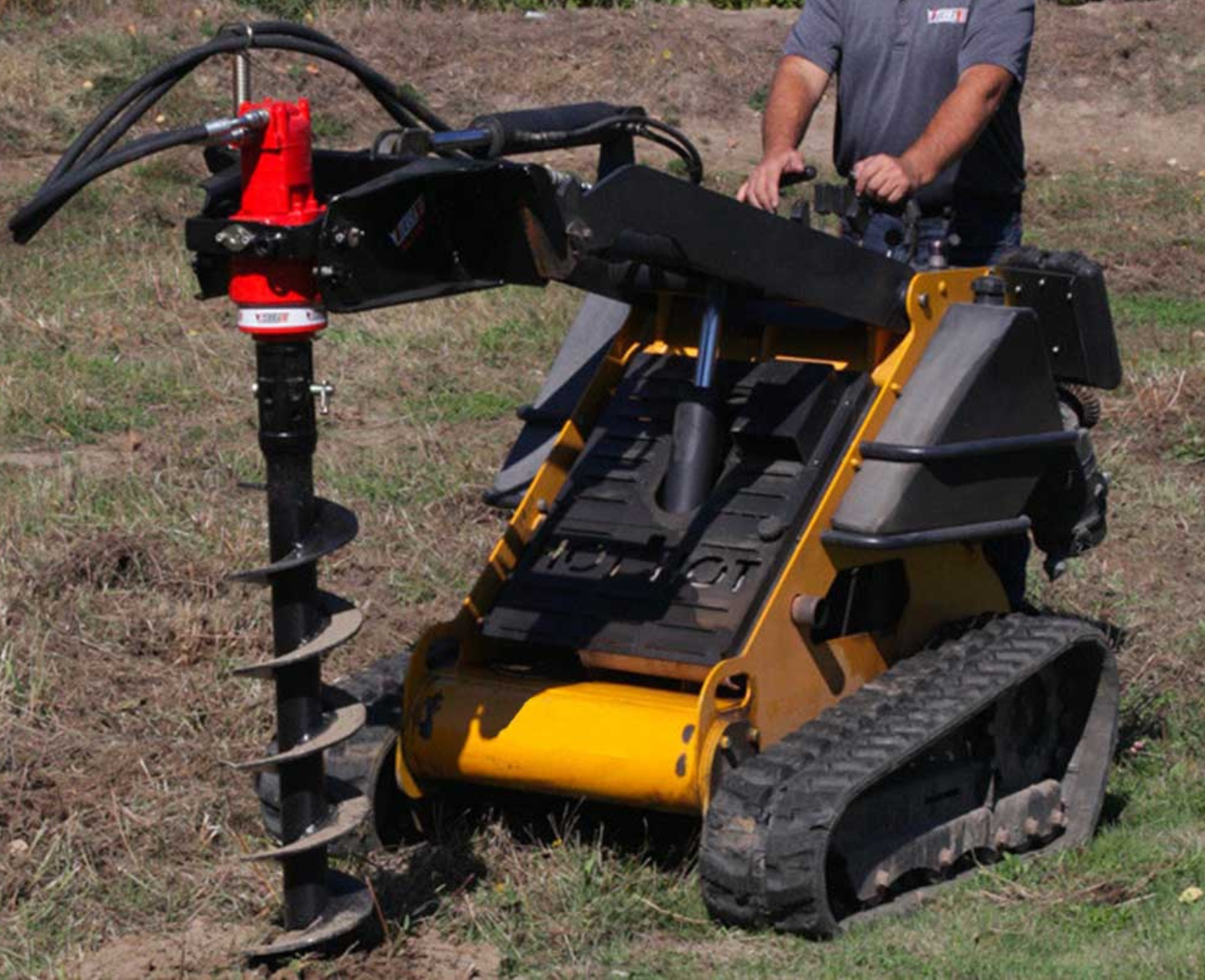 right angled view of a mini skid steer on grass with an eterra mini skid steer auger drive attachment on the front drilling into the ground