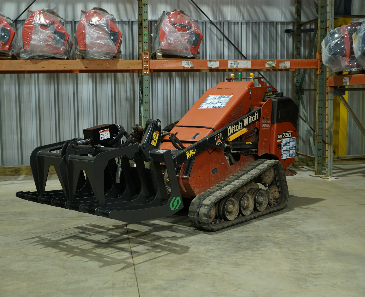 right angled view of a mini skid steer parked in a warehouse with a CID mini skid steer grapple attachment on the front slightly lifted