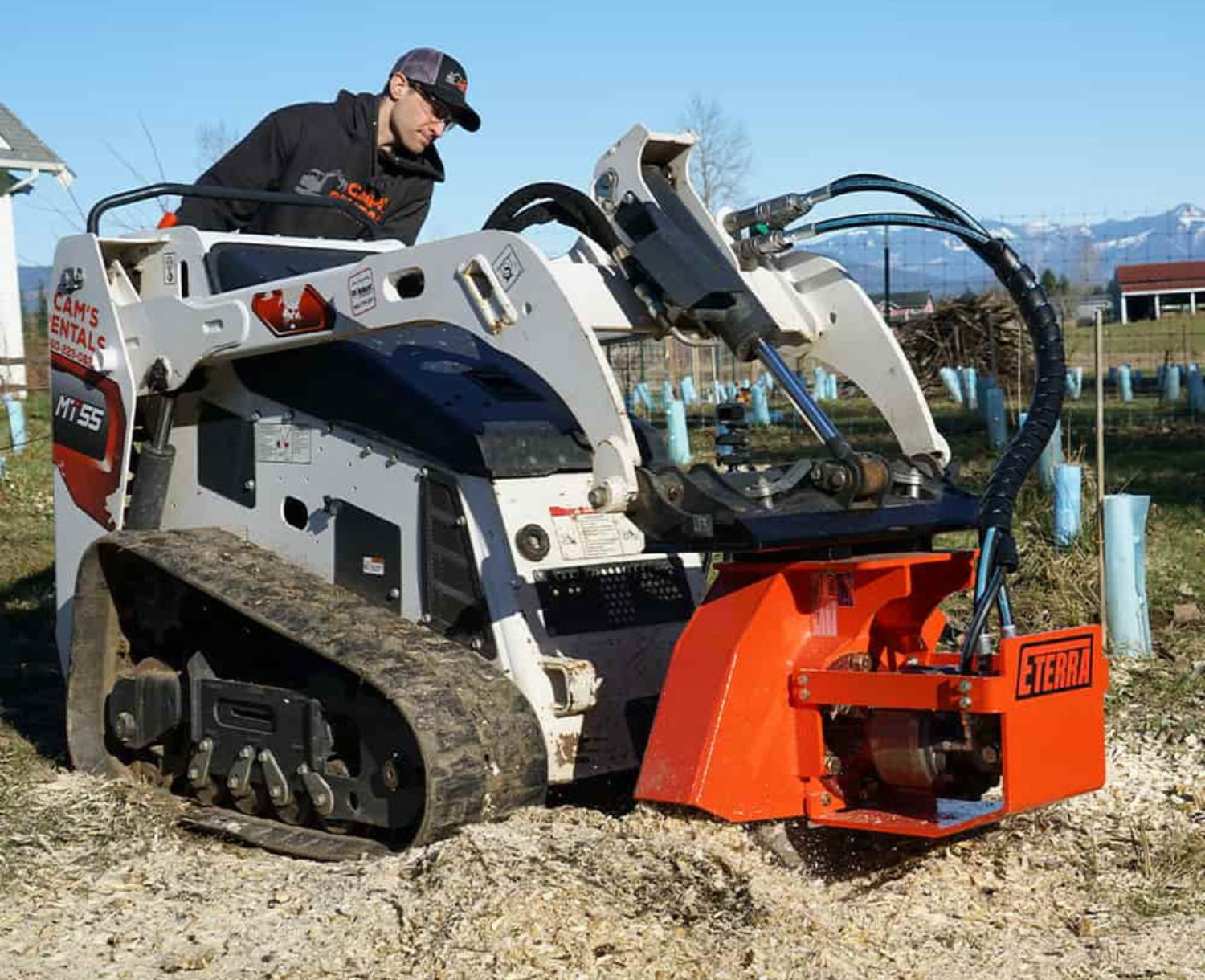 left anlged view of a mini skid steer parked on dirt with an eterra mini skid steer vortex stump grinder attachment on the front grinding