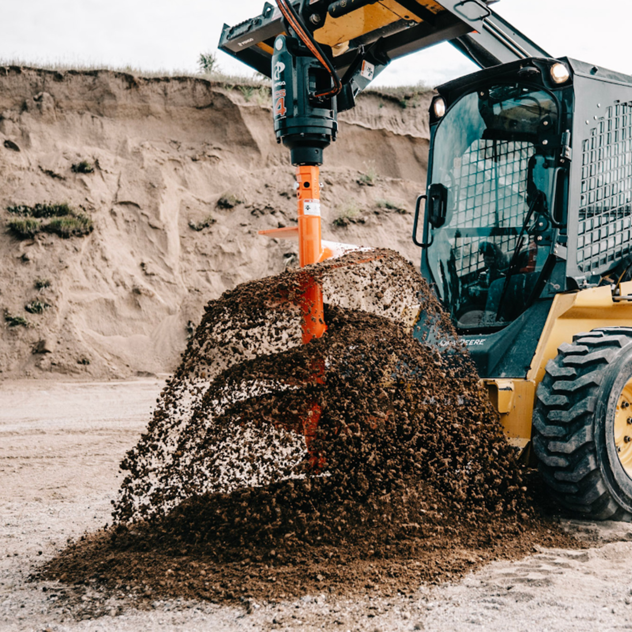 right angled view of a skid steer parked in a gravel pit spinning dirt off of a pengo skid steer auger attachment