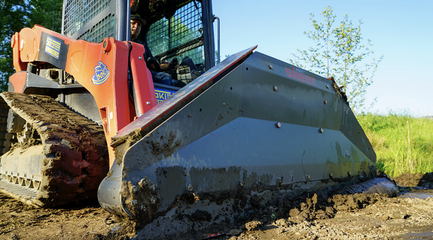 left angled view of a skid steer parked on dirt with a skeer skid steer precision grader attachment on the front