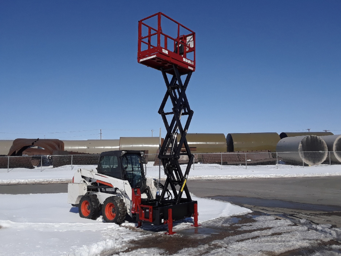 distant view of a skid steer parked at a left angle in a parking lot with a skid steer scissor lift on the front
