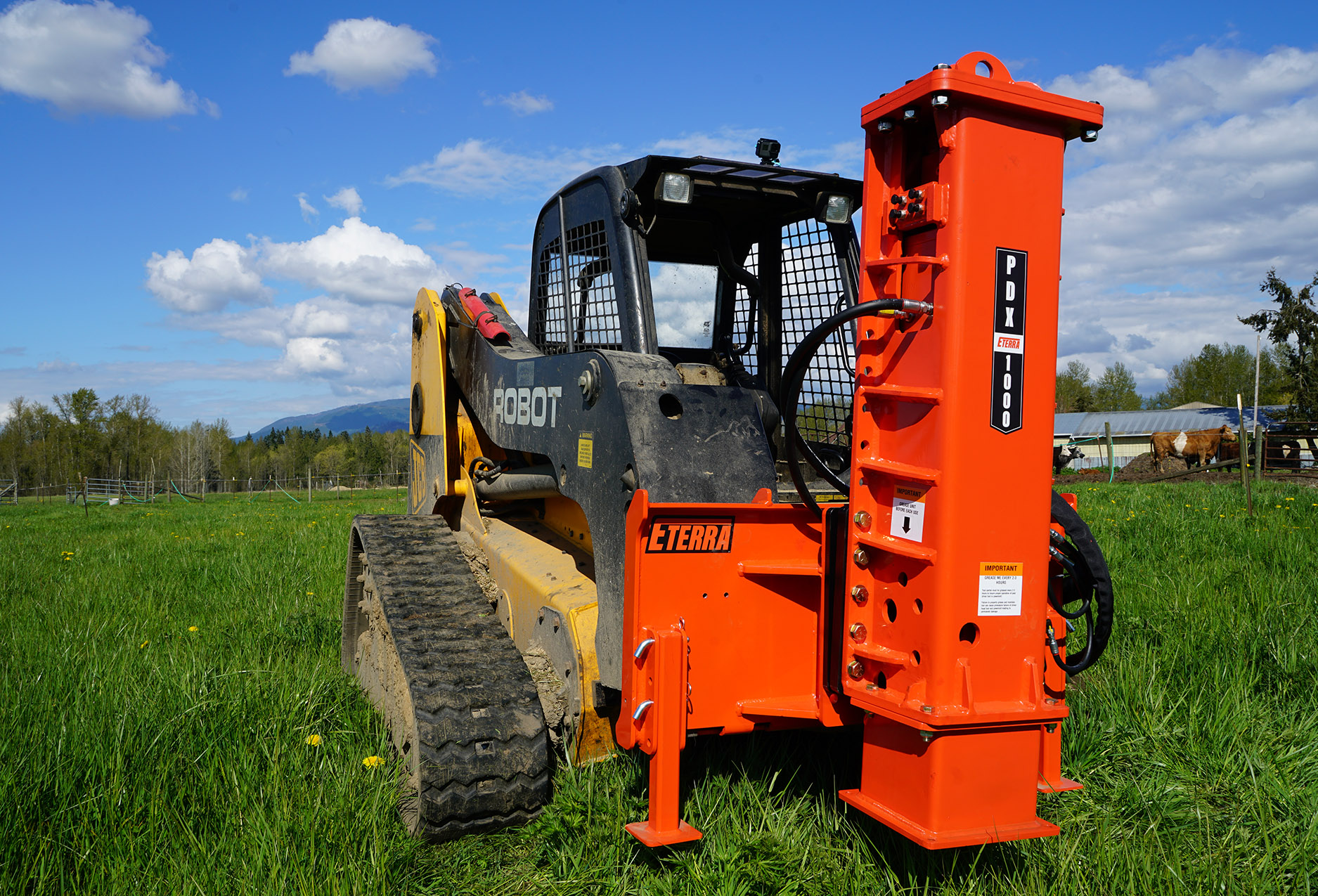 left angled view a skid steer parked on grass with an eterra pdx-1000 skid steer breaker style post driver attachment mounted on the front