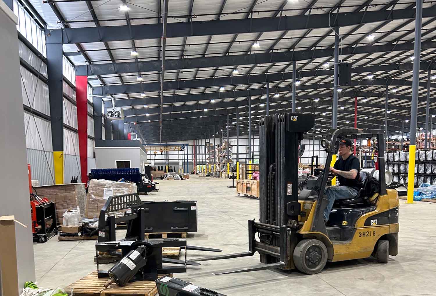 wide shot of skid steer solutions' warehouse with an employee moving a skid steer attachment with a forklift